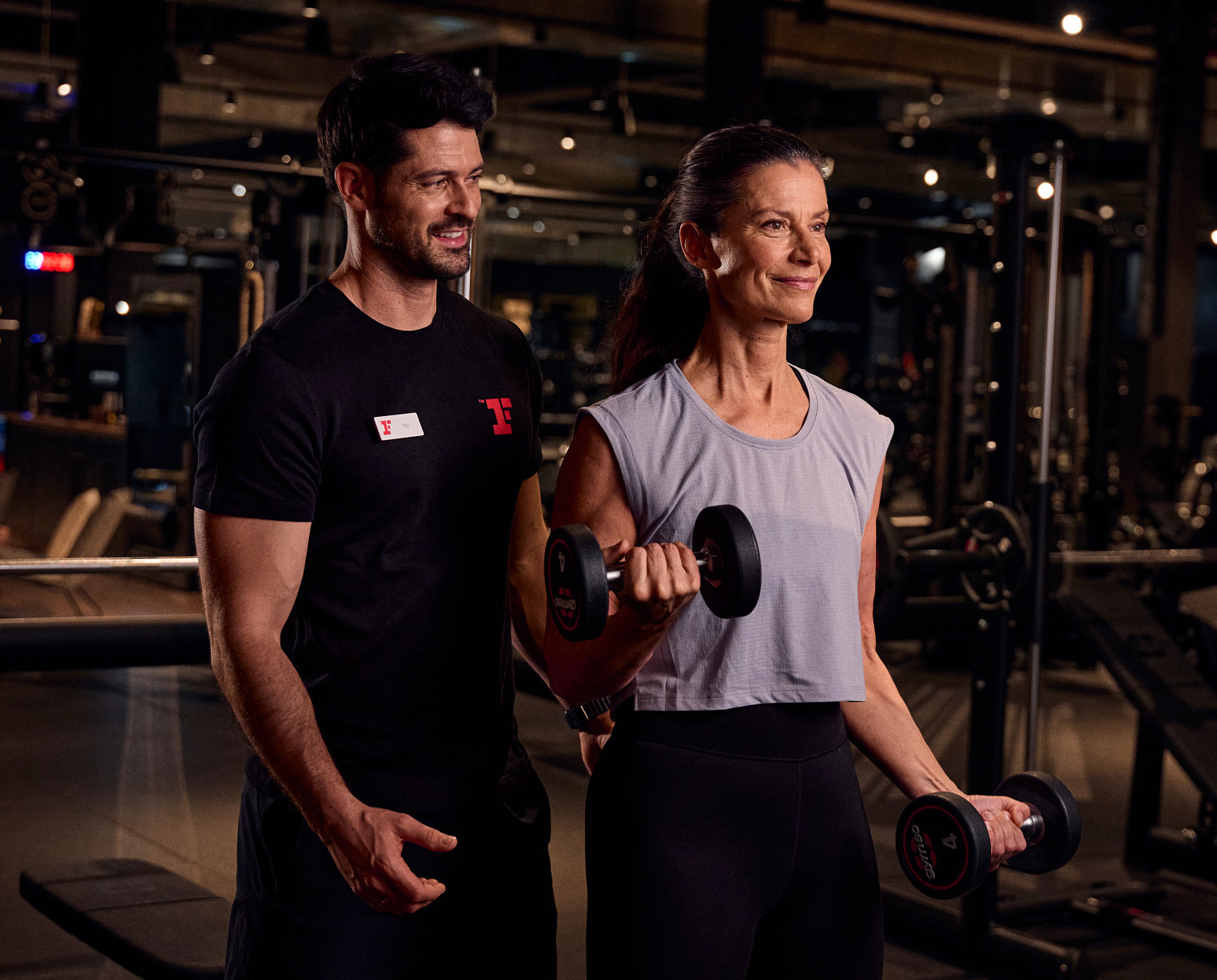 Trainer unterstützt Frau bei Freihanteltraining