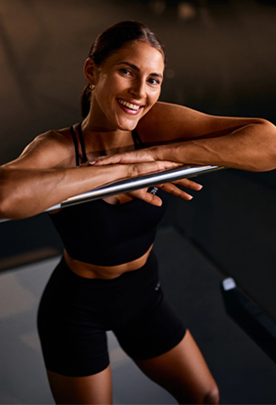 Fitness First Frau lehnt an Langhantel