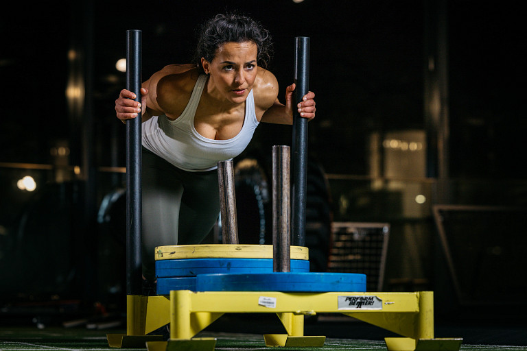 Frau schiebt Gewichtsschlitten beim Hyrox-Training bei Fitness First